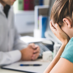Sad patient visiting doctor. Young woman with stress or burnout getting help from medical professional or therapist. Anxiety, depression or mental health problems concept.